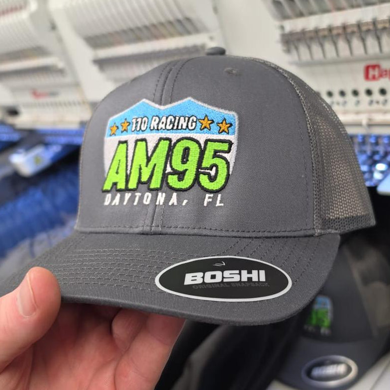 Gray cap with AM95 branding held in front of a sound mixing console.