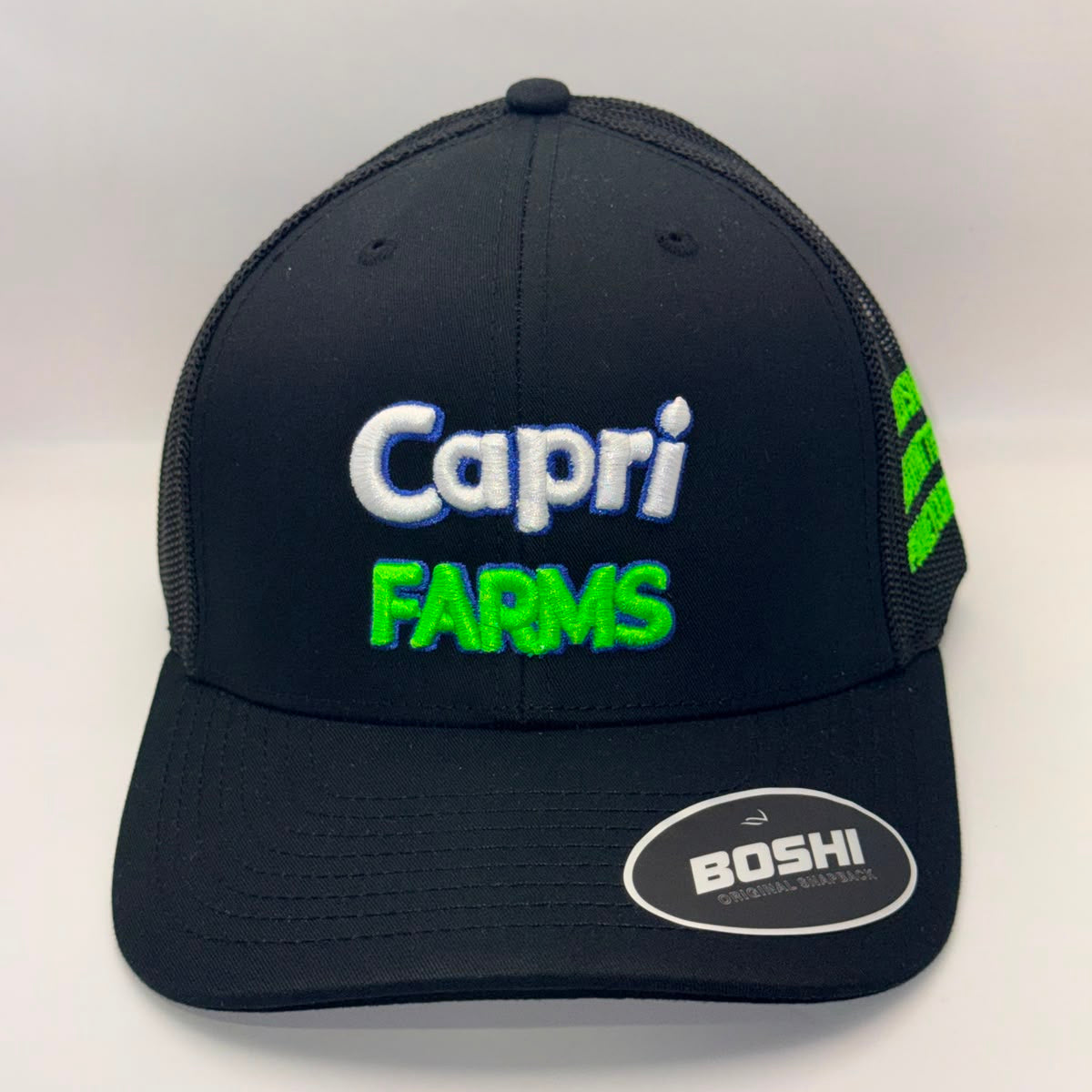 A black trucker-style baseball cap with 'Capri FARMS' embroidered on the front in white and neon green, featuring a visible BOSHI logo sticker on the brim and green embroidery on the side mesh.