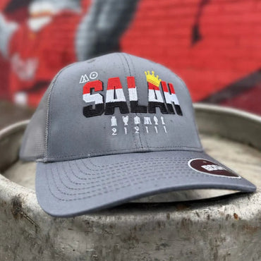Gray cap with 'MO Salah' branding on a concrete surface with graffiti in the background