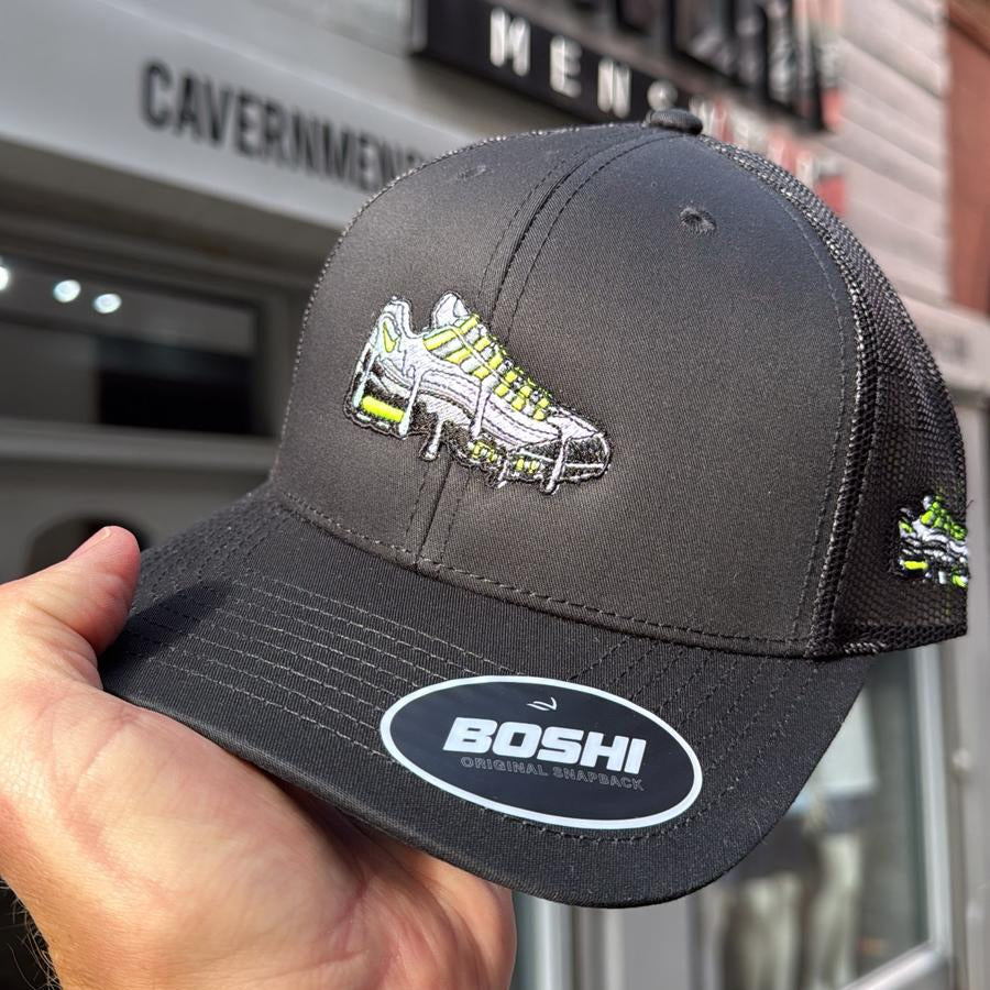 Black cap with green and white logo held in front of a building with 'Caubel' branding.