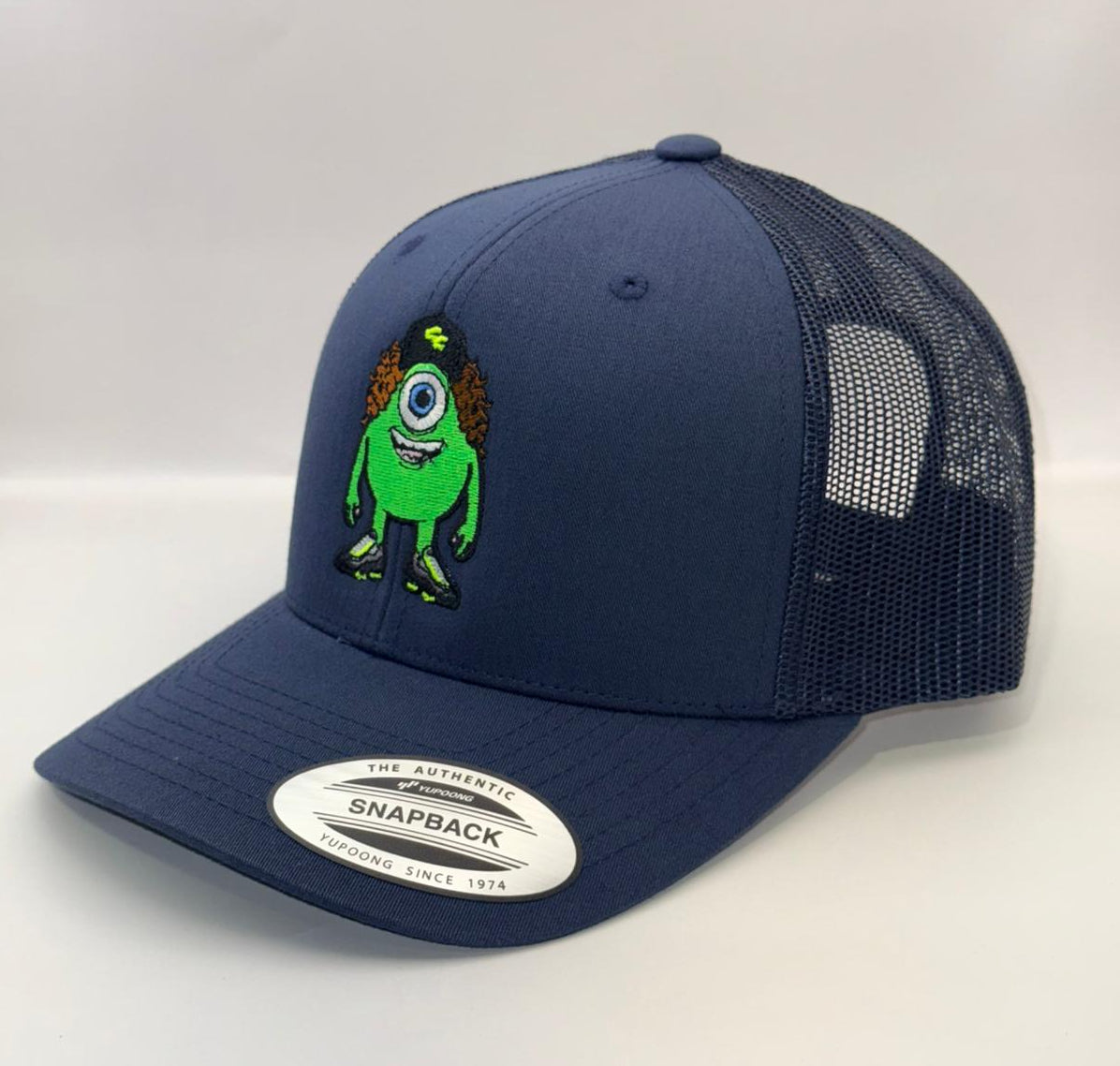 Navy blue snapback cap with a green character design on a white background