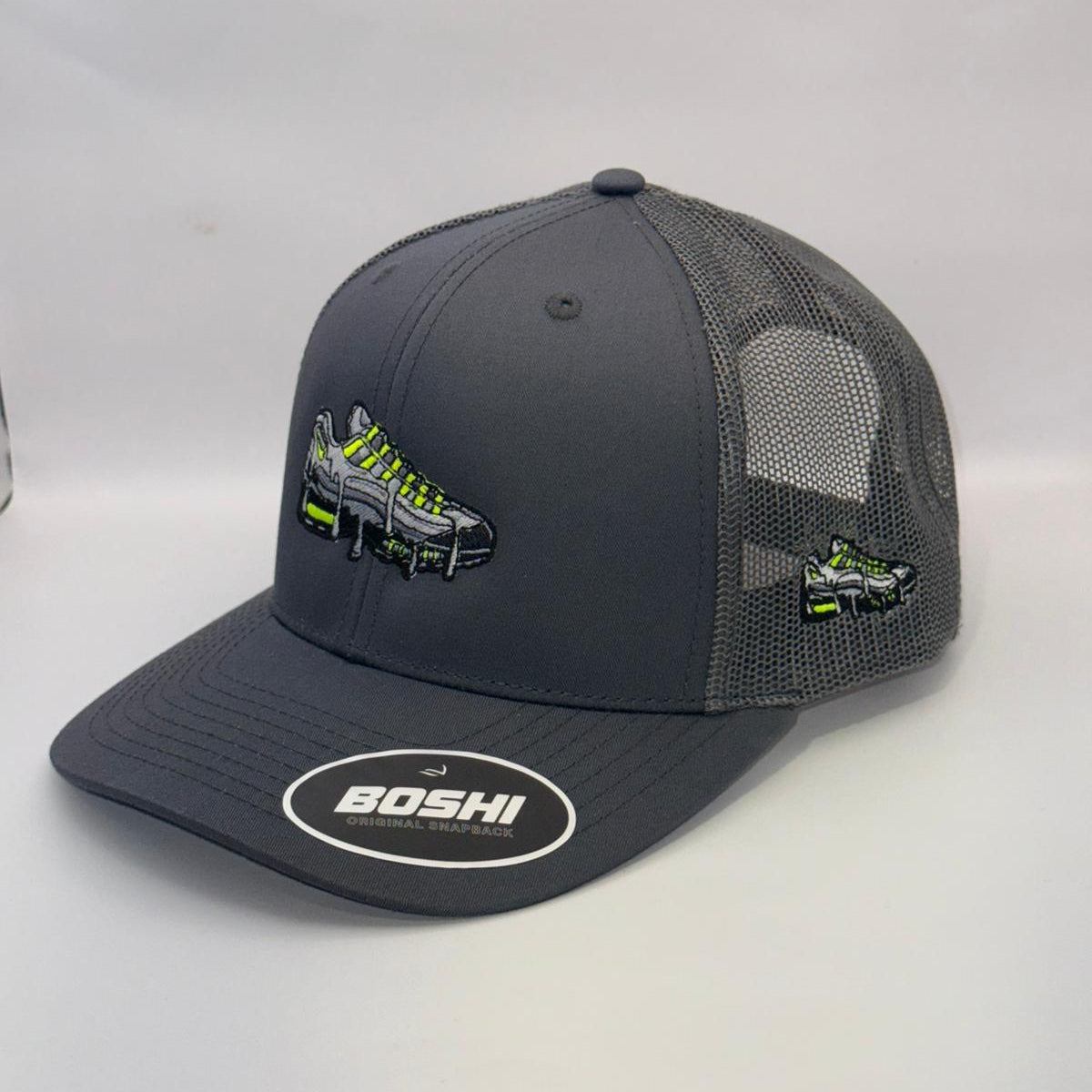 Gray trucker hat with mesh back and embroidered logo on a white surface