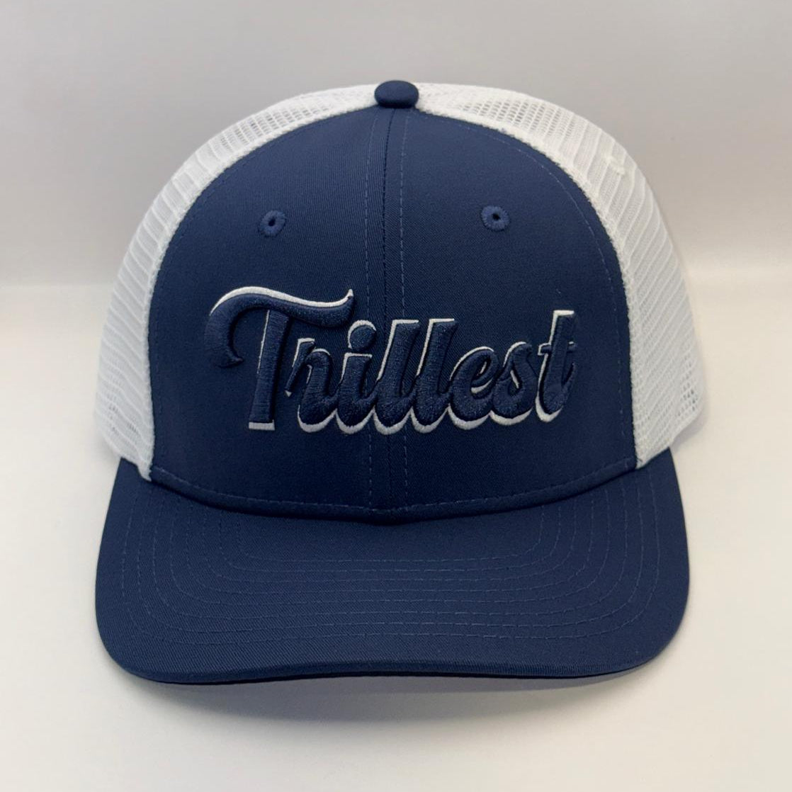 A navy blue and white trucker hat with 'Trillest' embroidered in navy script on the front, set against a plain light gray background.