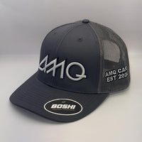 A dark gray AMQ trucker hat with a curved brim, featuring a white embroidered AMQ logo on the front, white text on the side mesh, and a circular white BOSHI logo patch on the brim.