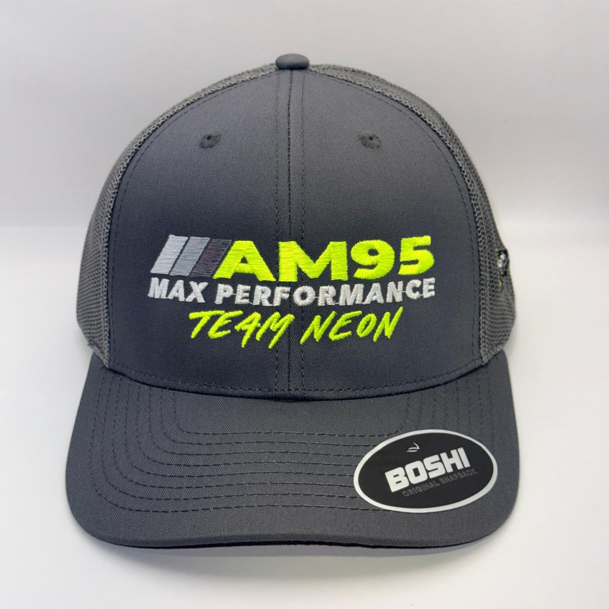 A dark gray trucker-style cap with mesh back panels, featuring 'AM95 MAX PERFORMANCE TEAM NEON' embroidered on the front in yellow and white, and a 'BOSHI' sticker on the brim.