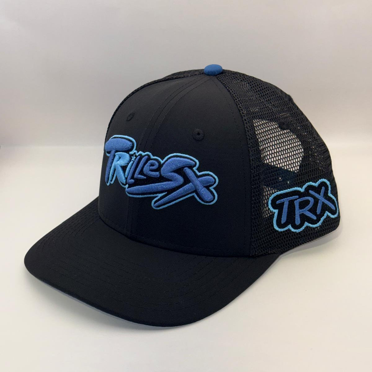 A black trucker-style cap with blue and white embroidered 'TRIX' logos on the front and side, set against a plain light background.