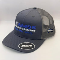 A dark gray and black mesh-back trucker hat with 'AM95 ALK PERFORMANCE' embroidered on the front in blue and white, featuring a white oval 'BOSHI' sticker on the brim and a small side patch.