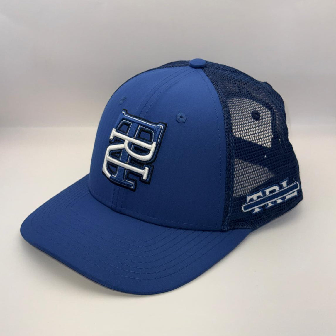 A royal blue trucker cap with a curved brim, featuring a blue front panel with a white and blue embroidered 'BC' logo, and a dark blue mesh back. A white 'MCI TIRE' logo is visible on the side mesh.
