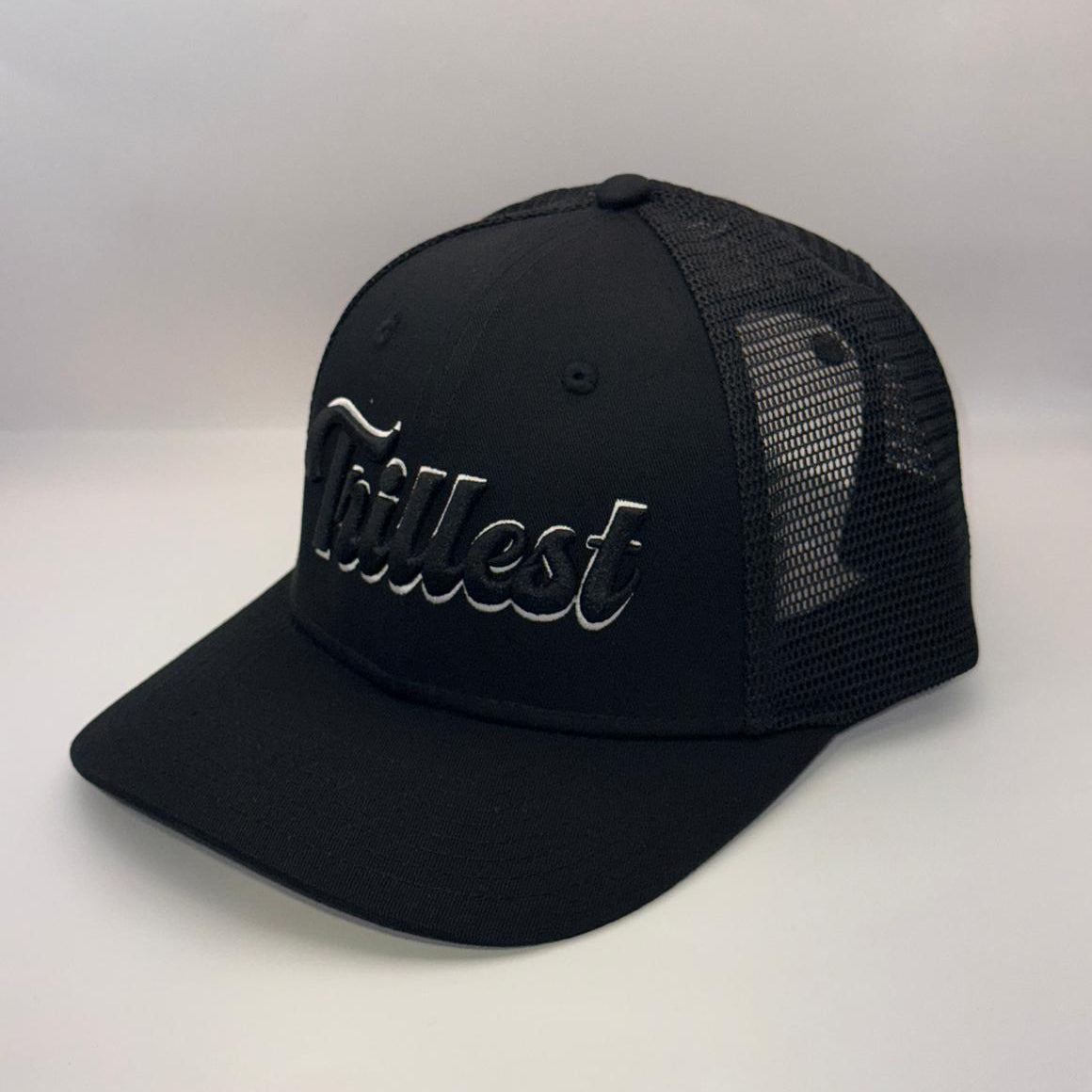 A black trucker-style cap with a curved brim, black mesh back panels, and a metallic silver cursive logo on the front that reads 'Tallest'.
