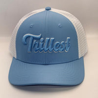 A light blue and white trucker hat with 'Trillest' embroidered in light blue script on the front, set against a neutral light gray background.