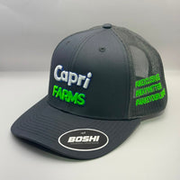 A dark gray trucker hat with 'Capri FARMS' embroidered on the front in white and neon green, featuring a matching neon green hashtag pattern on the side mesh. A white oval sticker on the brim reads 'BOSHI'.