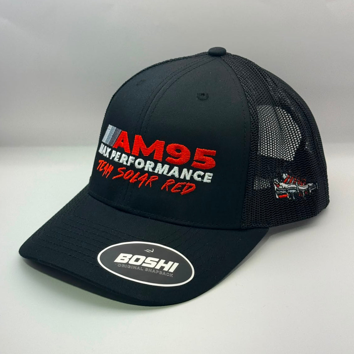 A black mesh-back trucker hat with a curved brim, featuring 'AM95 MX PERFORMANCE' and 'TEAM SOLAR RED' embroidered on the front in red and white, with a circular 'BOSHI' sticker on the brim.