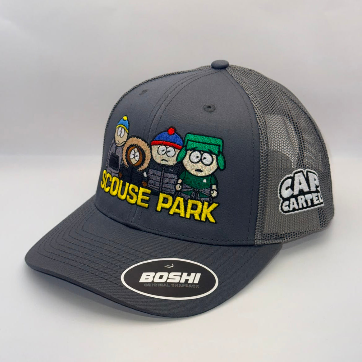 A dark gray trucker hat featuring South Park character graphics and 'SCOUSE PARK' text on the front, with 'BOSHI' branding on the brim and 'CAP CARTEL' on the side mesh.
