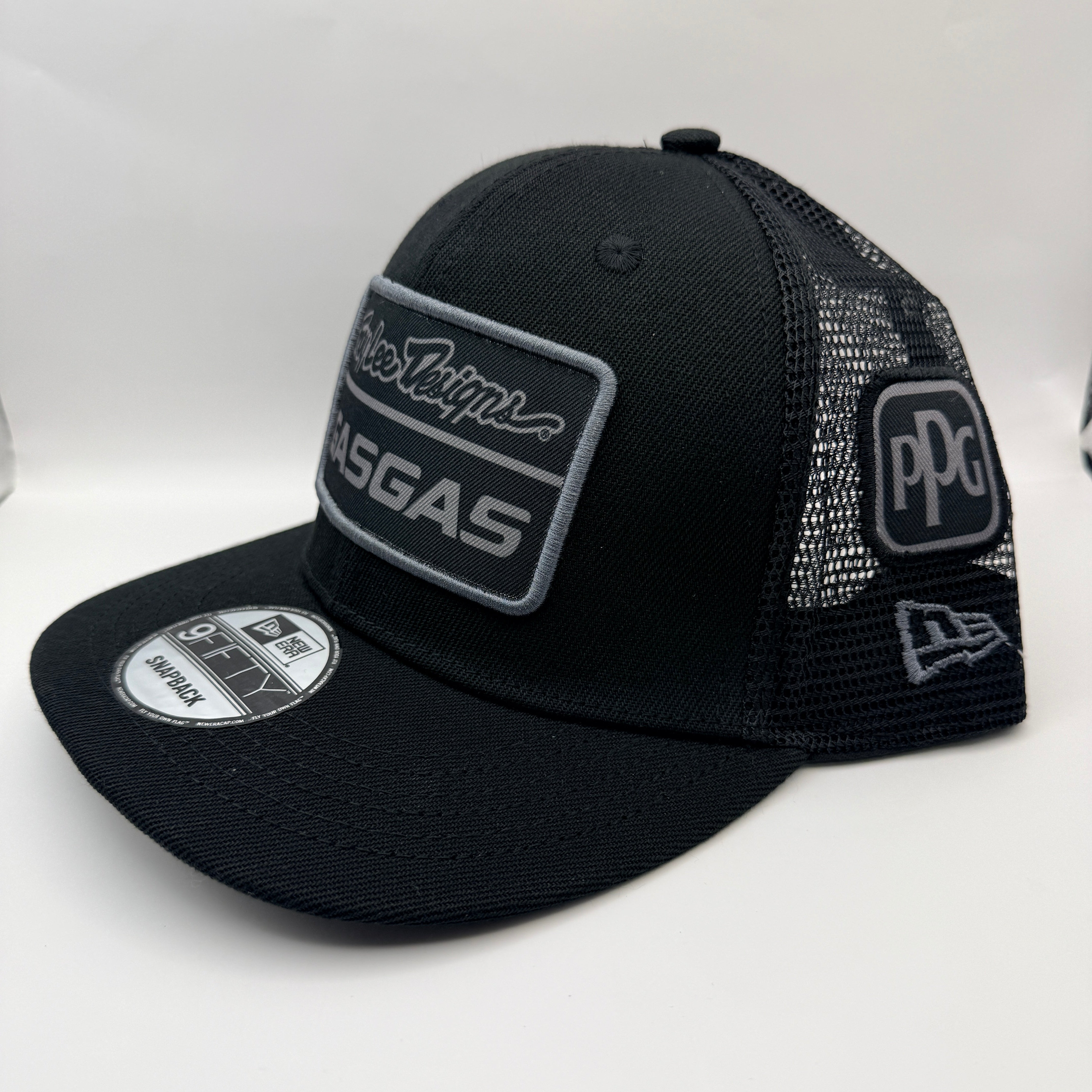A black trucker-style cap with a curved brim, featuring a rectangular patch on the front with 'KRGAS' and script lettering, a 'PPG' patch on the side mesh, and a New Era 9FIFTY sticker on the brim, set against a plain white background.