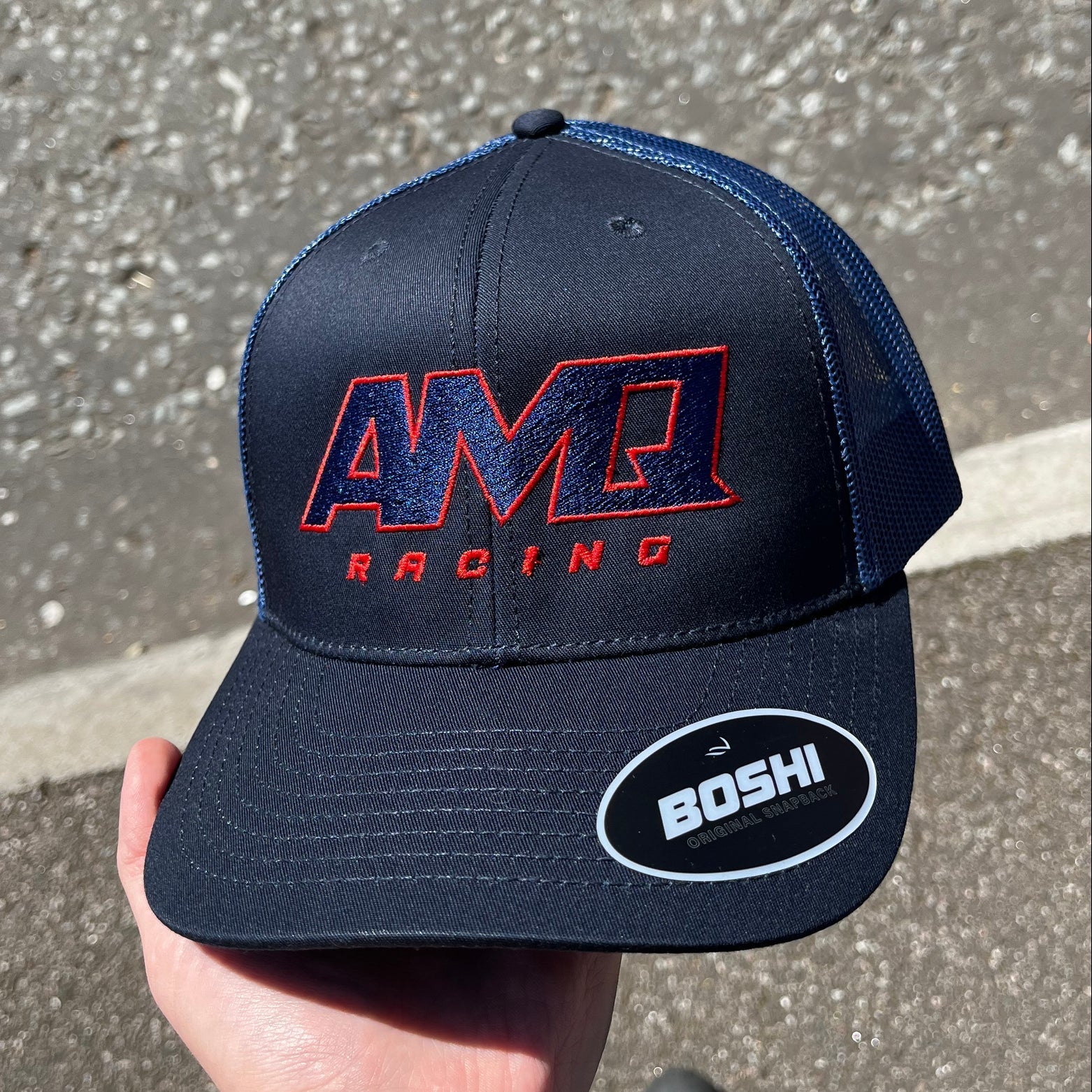 Navy blue cap with red and white text held by a hand on a concrete surface